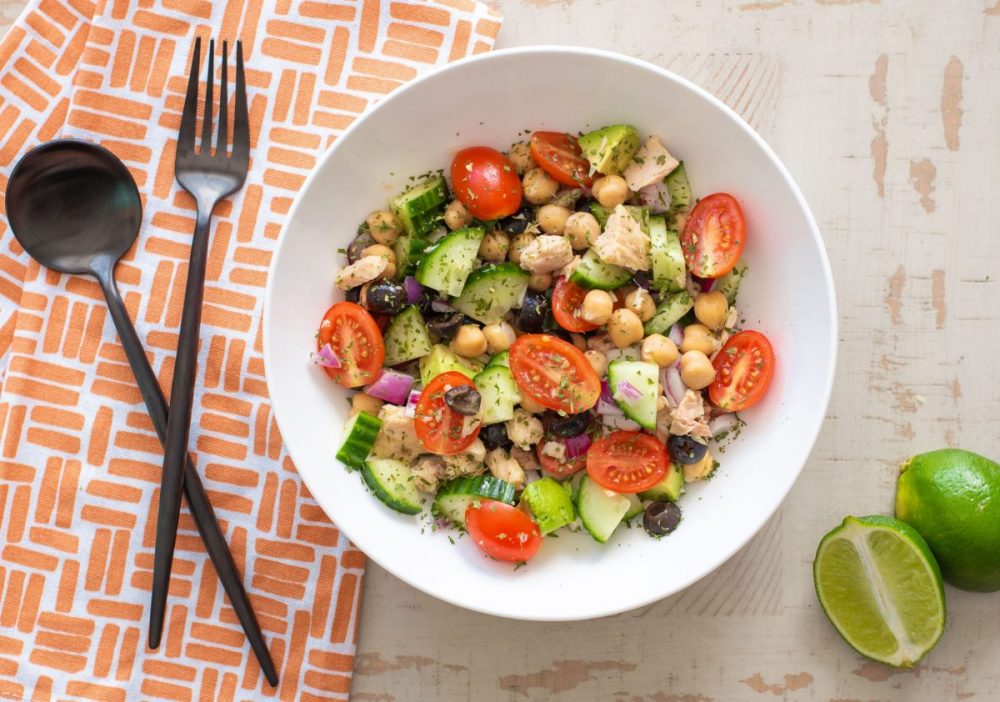 Mediterranean Salad with tomatoes, cucumbers, tuna and chickpeas in white bowl next to orange napkin