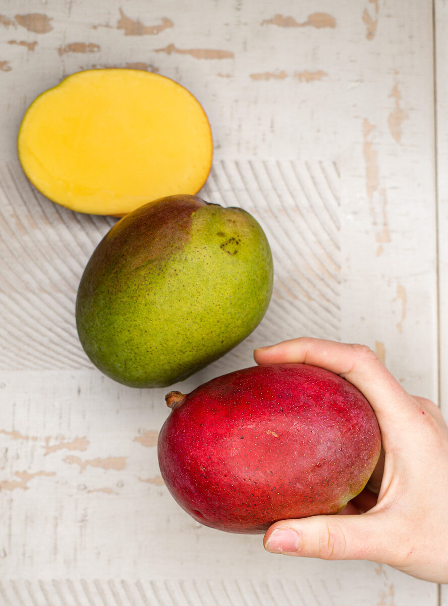 two ripe mangos, one cut in half, one whole