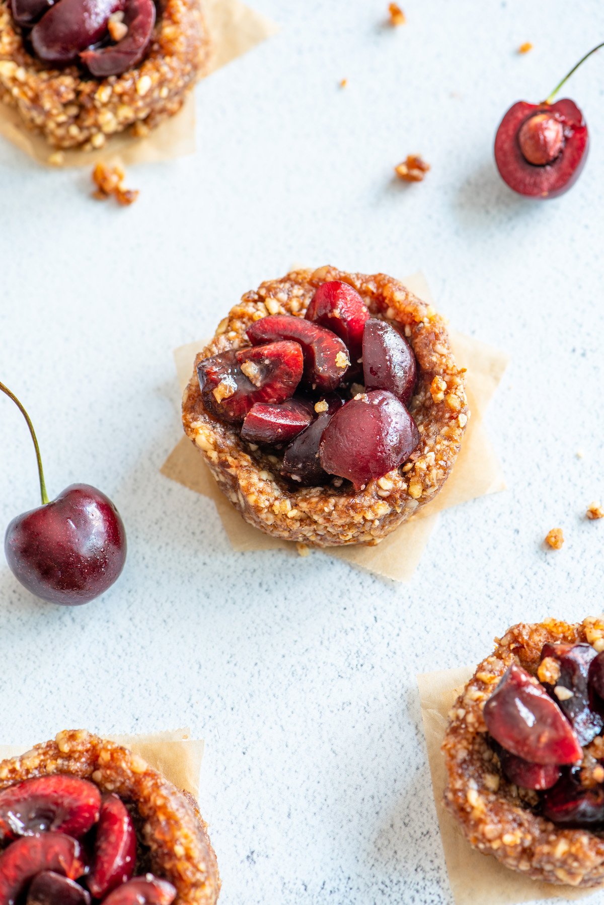 four mini cherry pies on a white background with a whole and pitted cherry