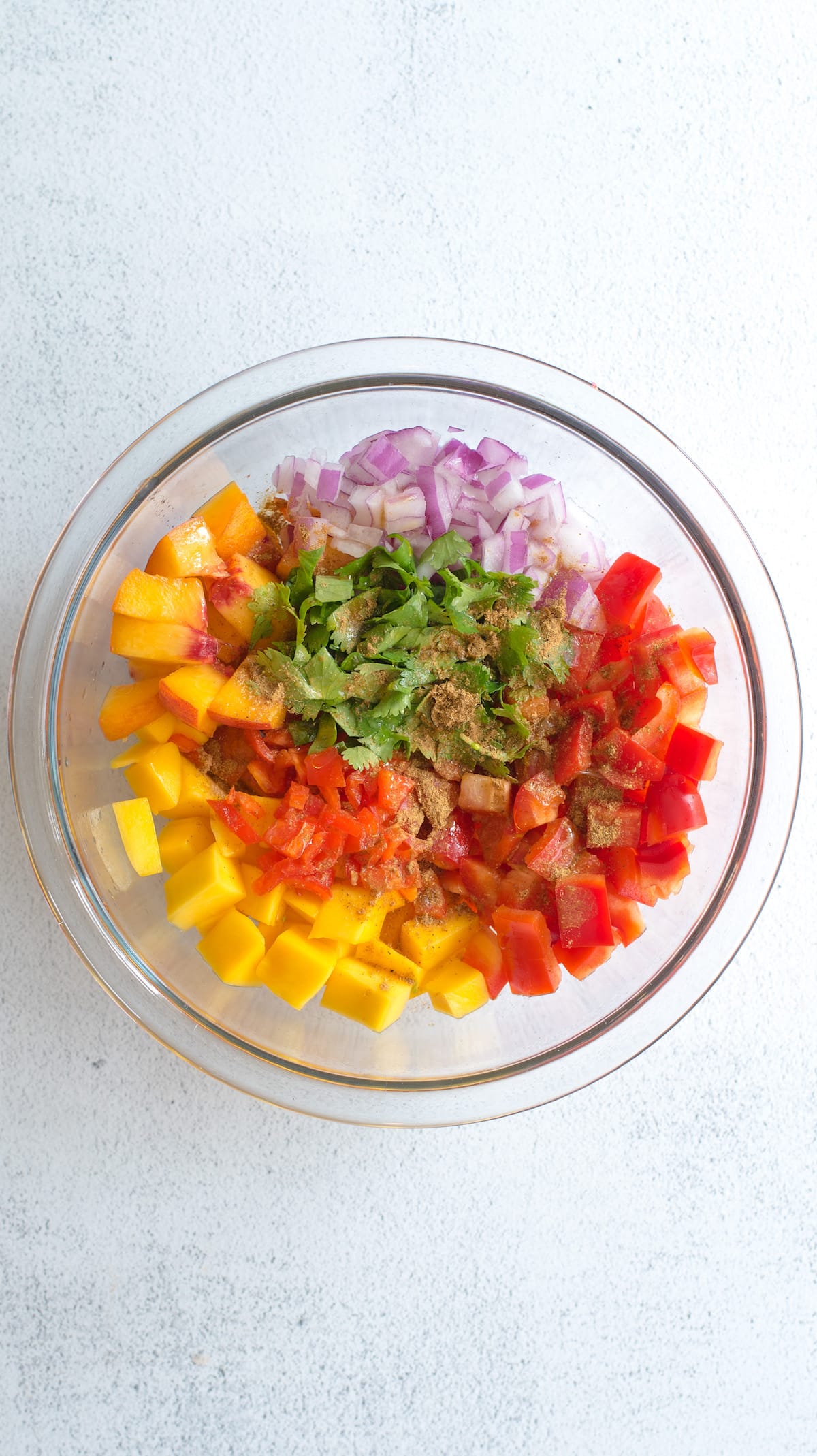 bowl of unmixed salsa ingredients covered in cumin, salt, and pepper