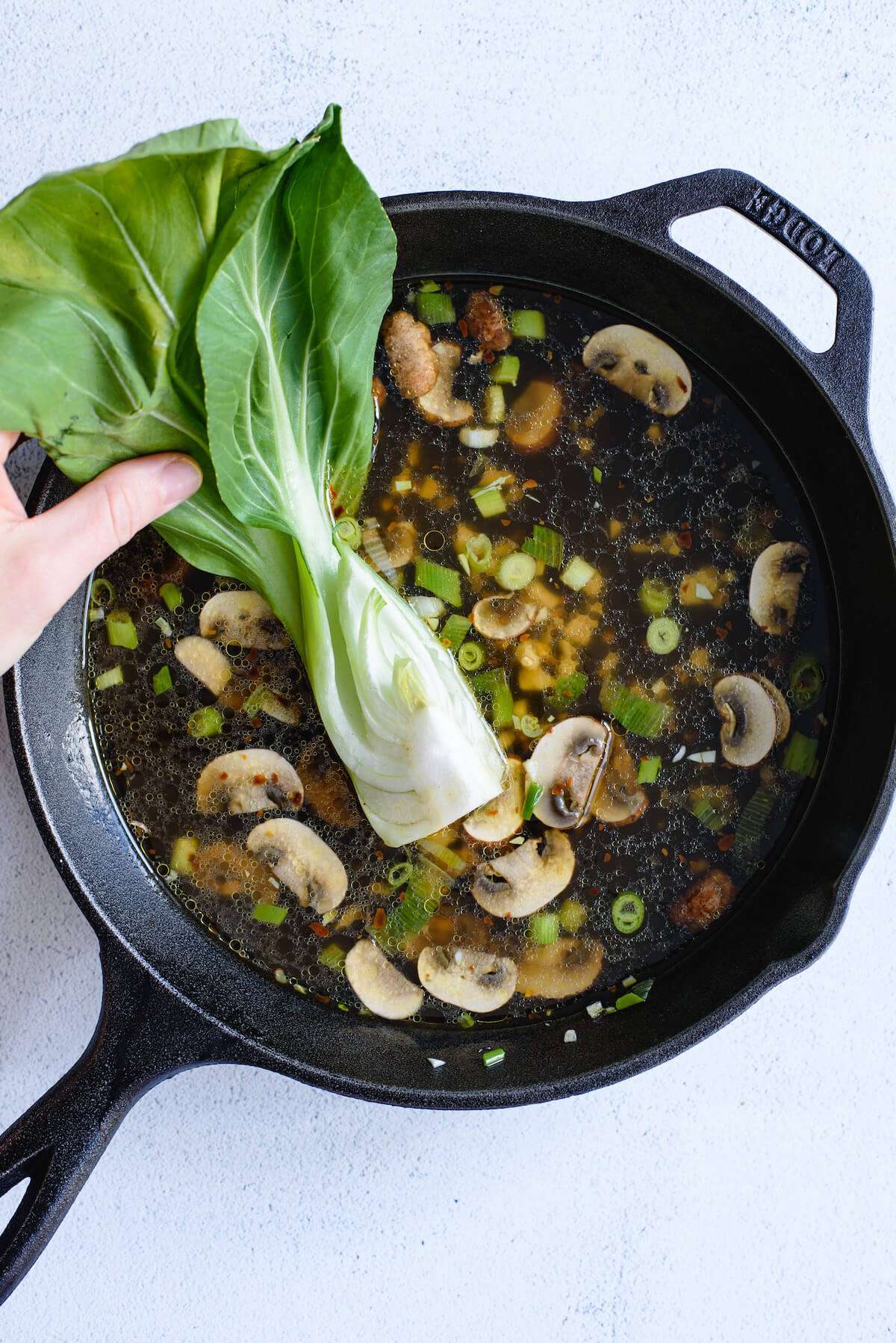 hands placing bok choy into soup