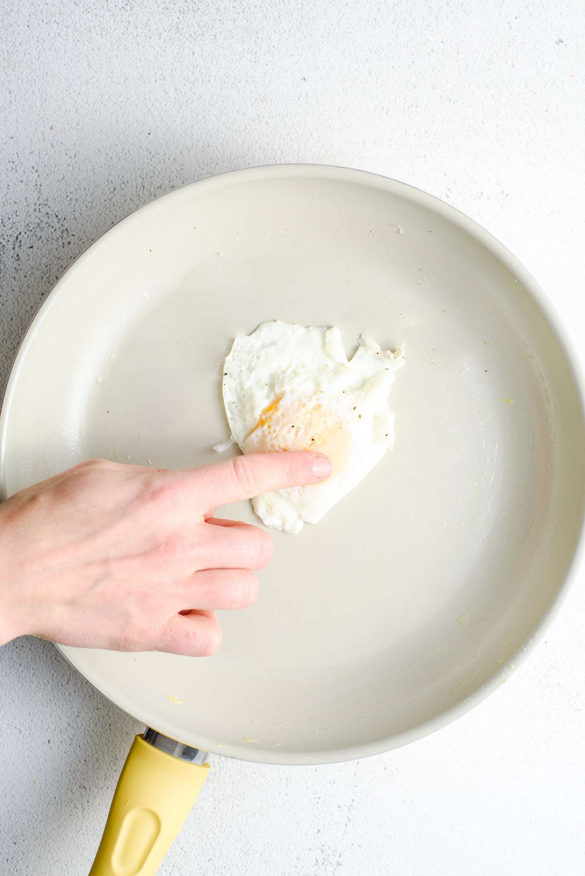 hand pressing egg yolk to check doneness 