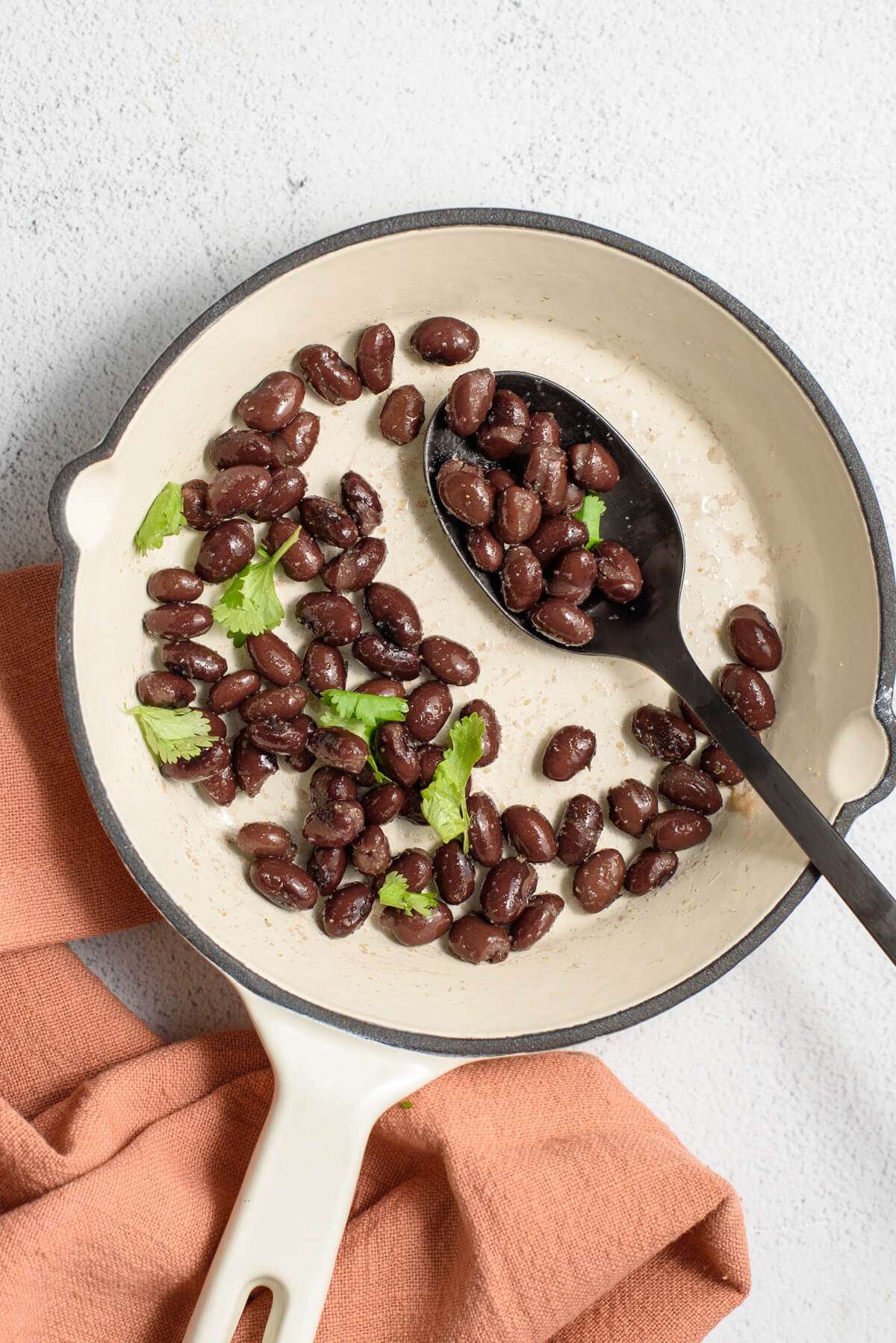 canned black beans cooking on skillet with seasoning, cilantro, and a spoon