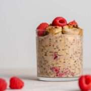 raspberry banana overnight oats in a glass surrounded by raspberries