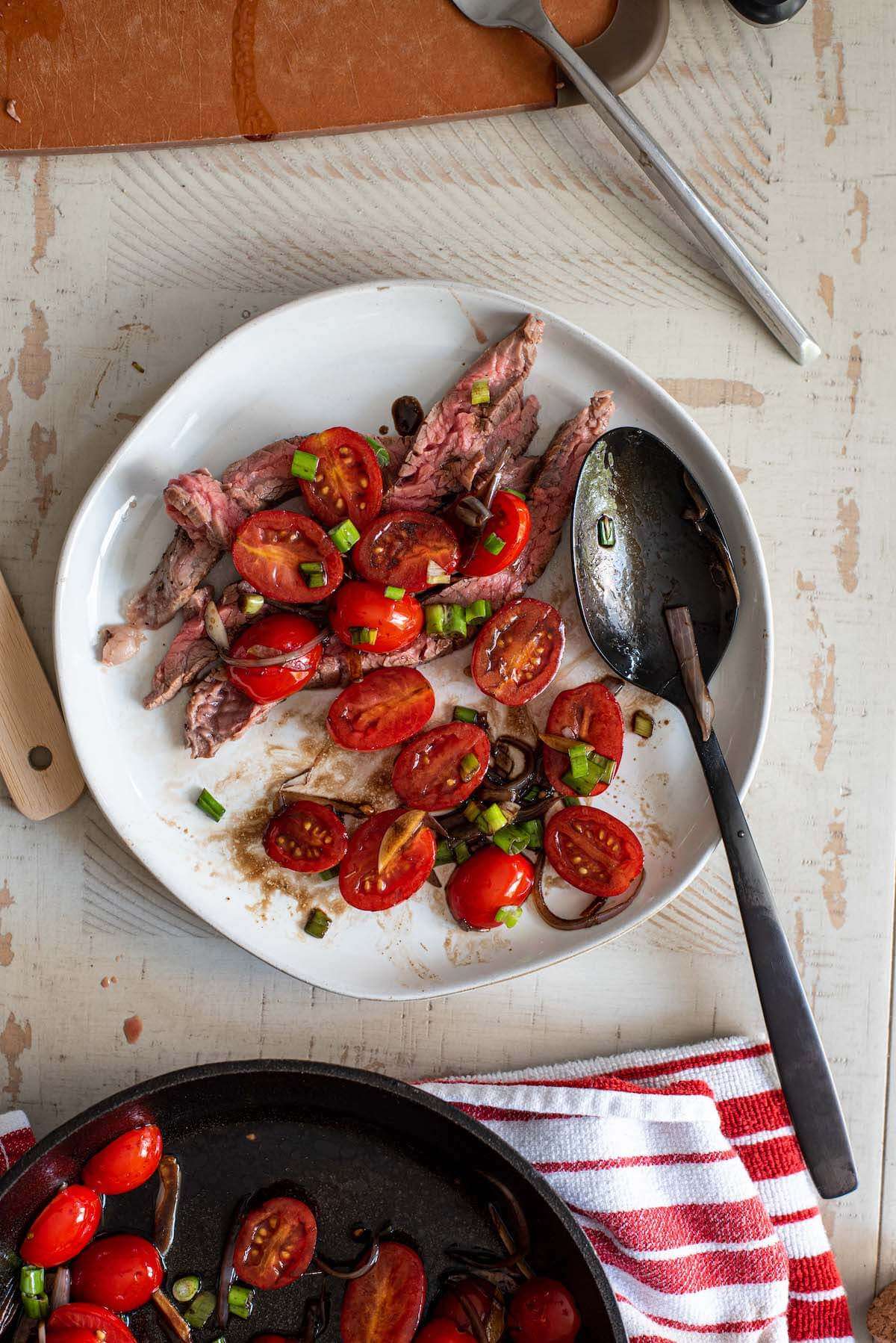 plate of sliced flank steak with balsamic tomatoes