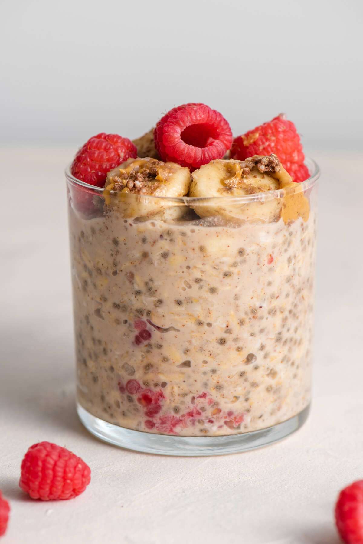 jar of overnight oats topped with raspberries, banana slices, peanut butter, and crushed undercover quinoa