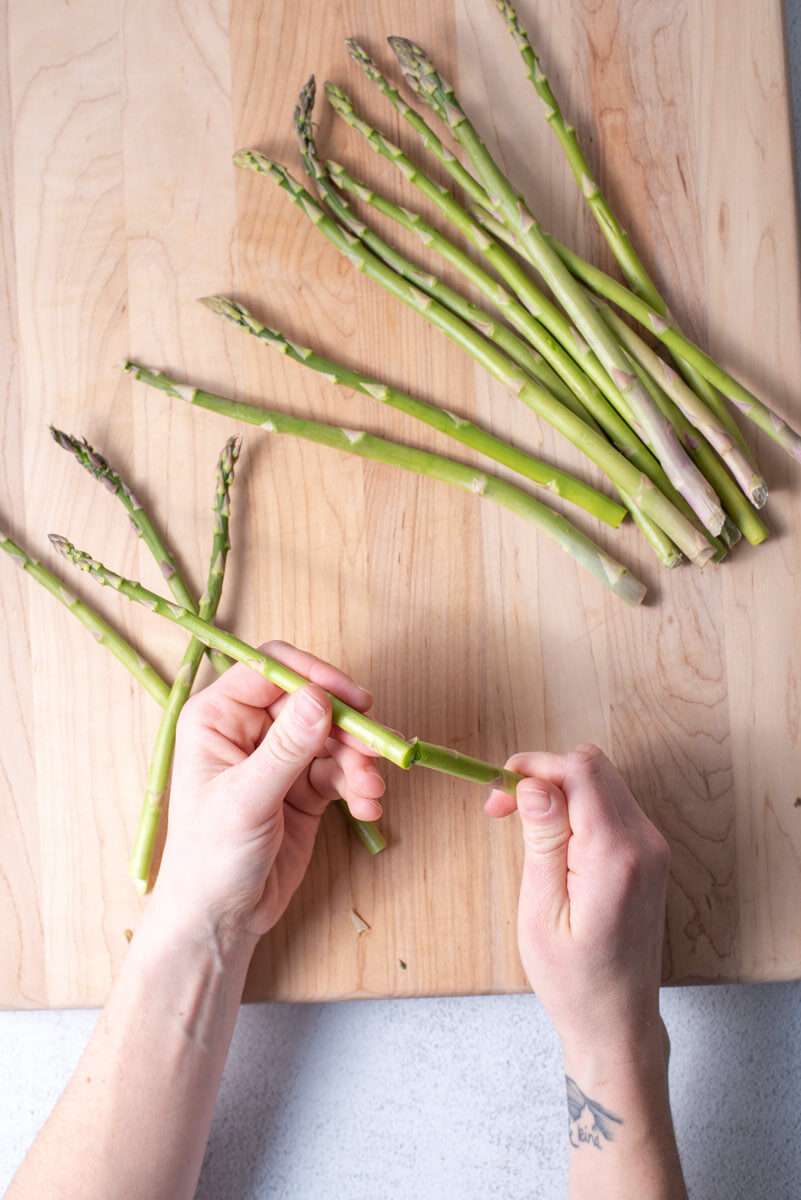 hands snapping the ends of asparagus spears on a cutting board