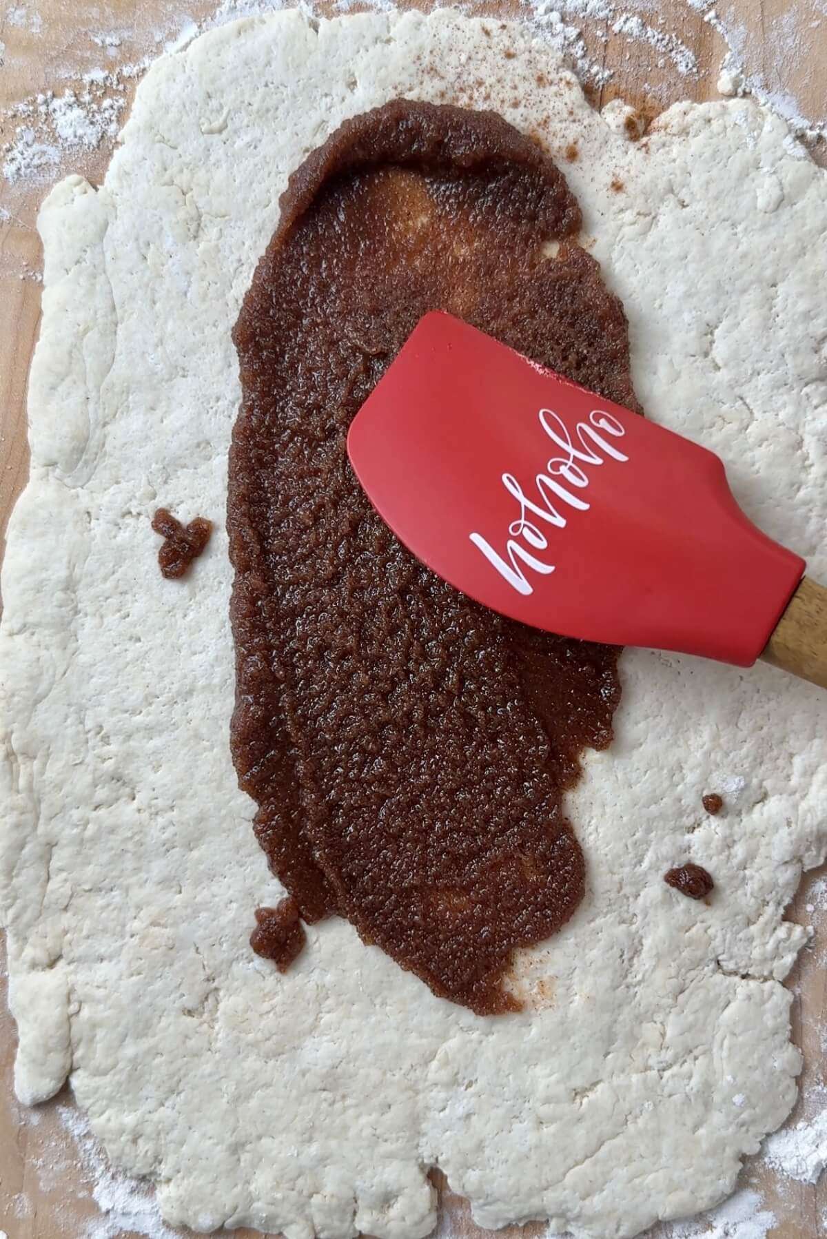 spatula spreading cinnamon roll filling over dough