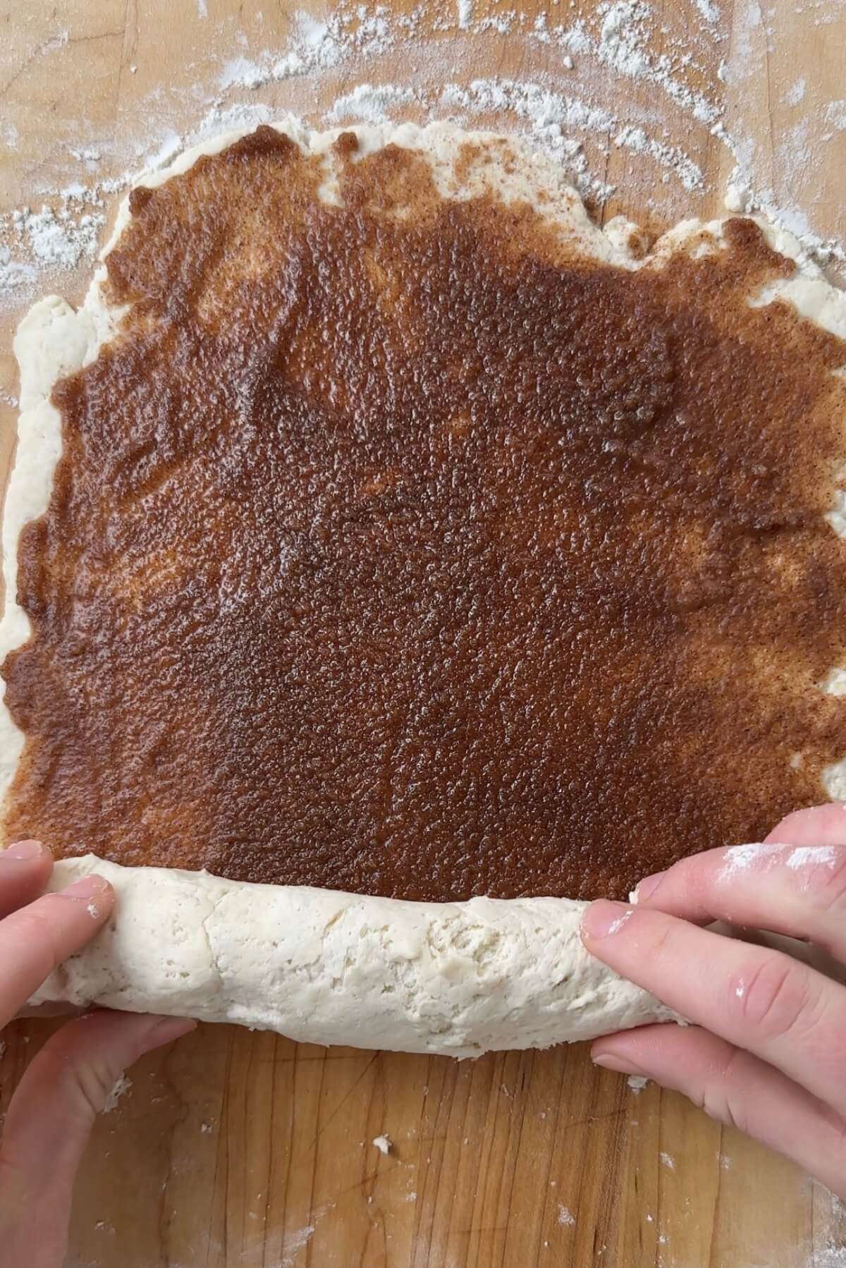 hands rolling the shorter end of rectangular cinnamon roll dough