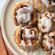 protein cinnamon rolls on white plate with pink napkin covered in icing