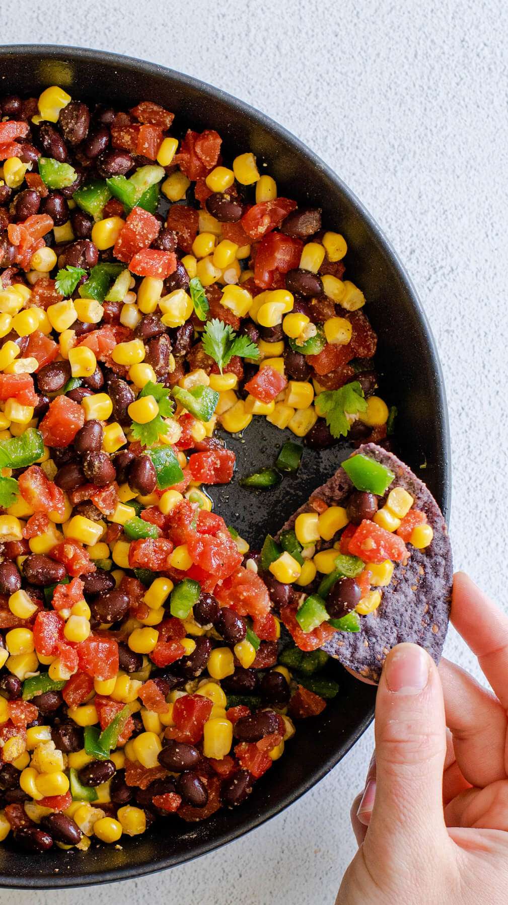 hand scooping black bean salad with blue corn tortilla chip