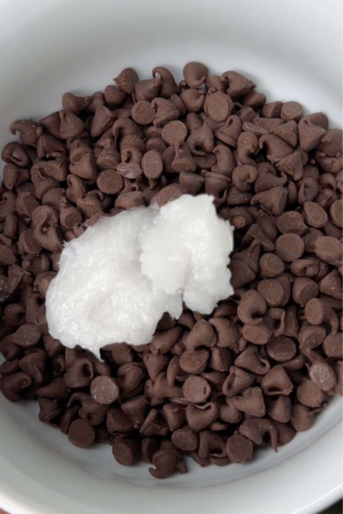 dark chocolate chips in a white bowl with coconut oil